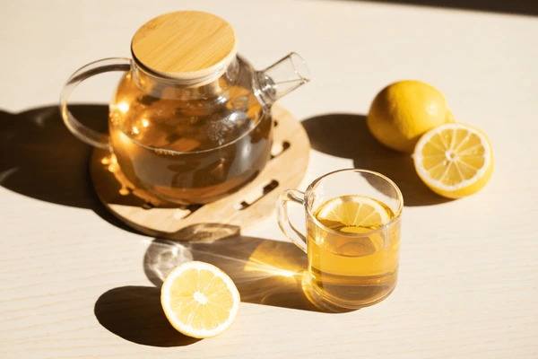 Freshly brewed lemon tea in a glass teapot and cup with sliced lemons, showcasing a soothing herbal tea rich in vitamin C.