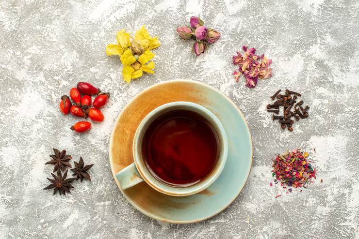 Cup of herbal tea surrounded by dried flowers, spices, and herbs on a textured background.
