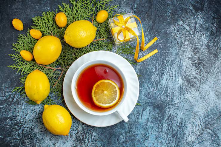 Overhead view of black tea with lemon slice in a white cup, surrounded by fresh lemons and citrus on a dark textured background