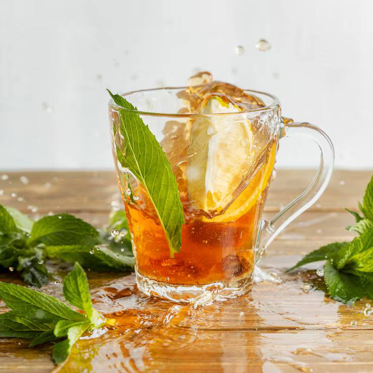 Refreshing herbal iced tea with lemon slices and fresh mint leaves in a glass mug, splashing over ice for a cooling summer tea drink.