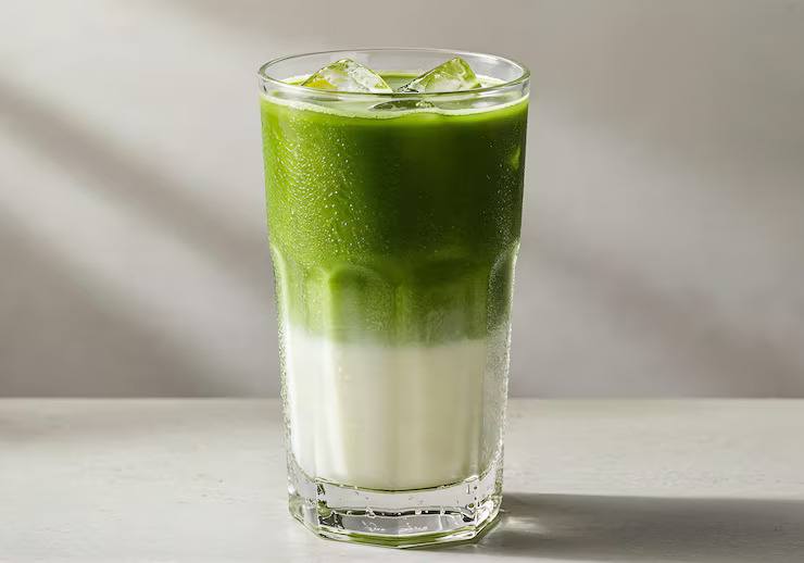 Layered matcha iced tea with milk and ice cubes in a tall glass, featuring a refreshing green tea latte style beverage.