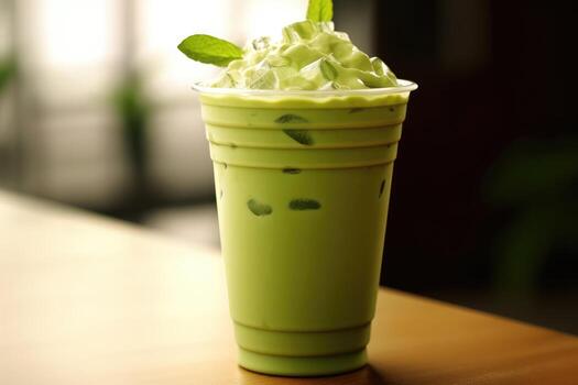 Creamy green iced tea topped with whipped foam and fresh mint, served chilled in a takeaway cup, showcasing a refreshing matcha-style iced tea beverage.