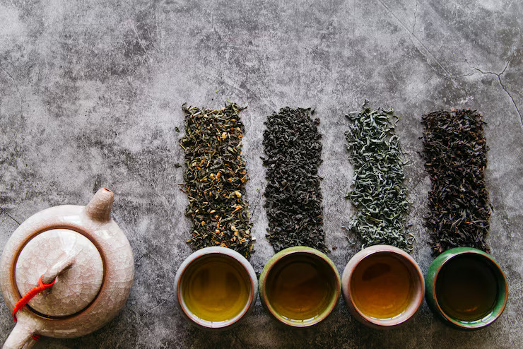 Assorted tea types displayed with loose leaf black, green, oolong, and herbal teas alongside brewed tea cups and a traditional teapot.