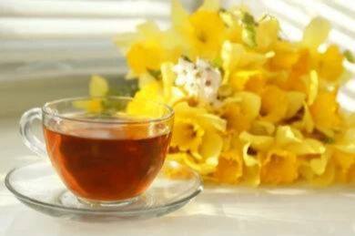 Glass cup of Narcissus tea served beside fresh yellow flowers in natural daylight.