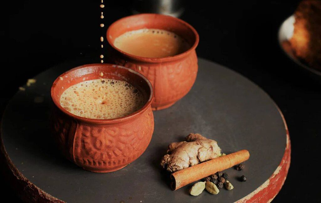 Authentic Indian masala chai served in handmade clay cups with spices like ginger, cinnamon, cardamom, and pepper placed beside them.