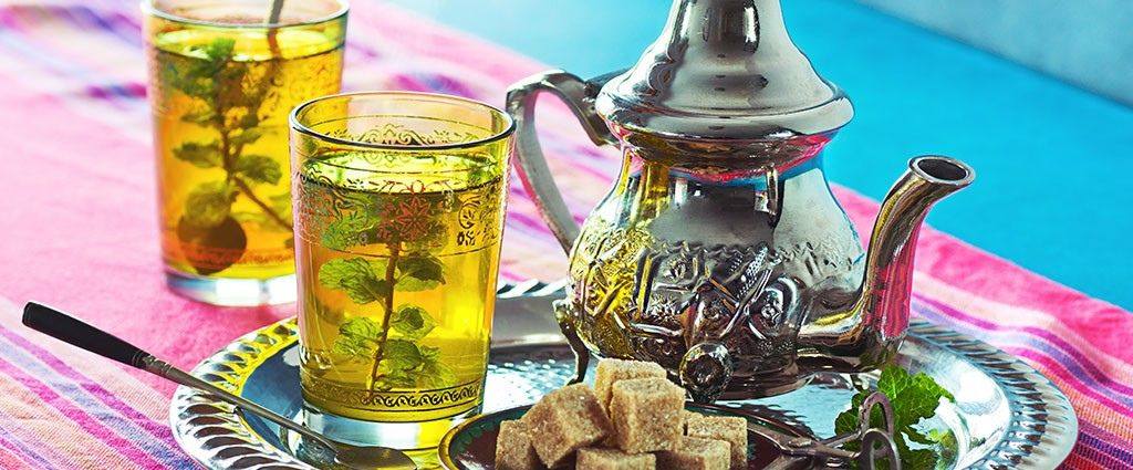 Traditional Moroccan mint tea served in ornate glasses with fresh mint leaves, alongside a decorative silver teapot and sugar cubes.