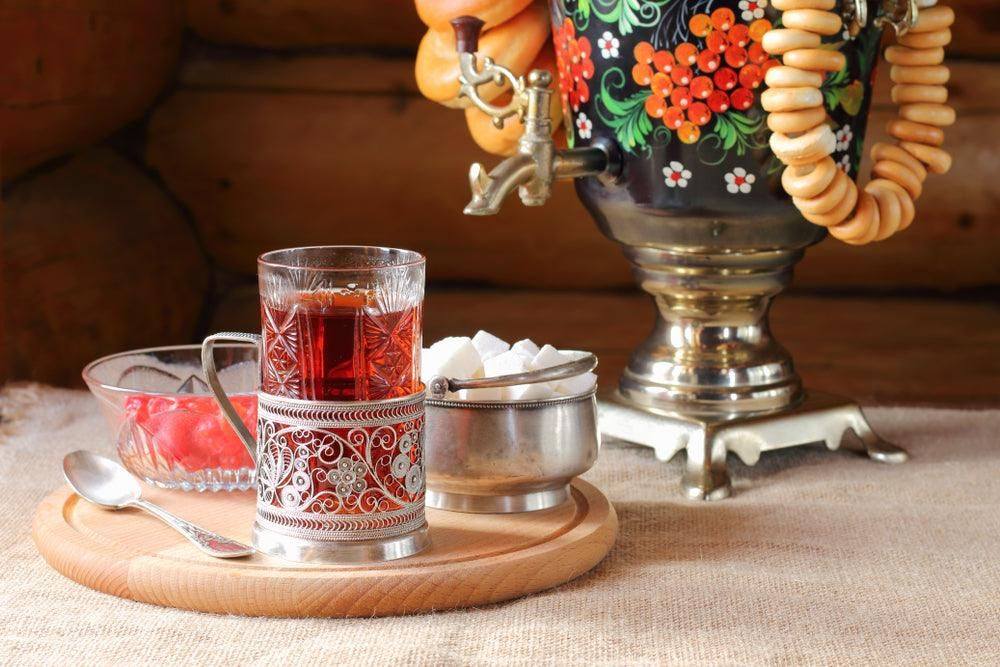 Traditional Russian tea setup with a samovar, a glass of black tea in an ornate metal holder, sugar cubes, and tea snacks.